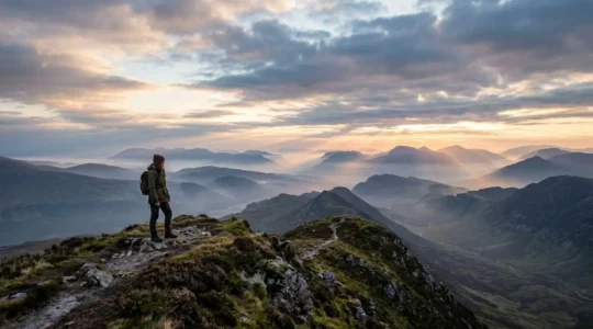 Solo traveler contemplating misty Scottish Highlands at dawn